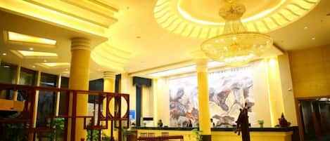 A hotel lobby with a large chandelier, a reception desk, and a large mural on the wall.