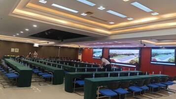 A conference room with rows of tables and chairs, a large screen, and a projector.
