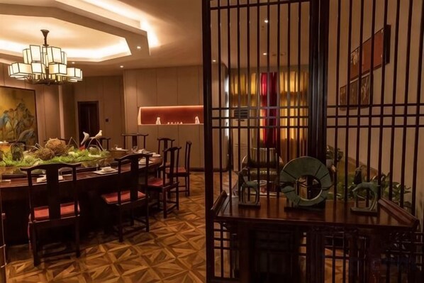 Un comedor de hotel con una mesa redonda, sillas, un centro de mesa decorativo y una separador con barras verticales.