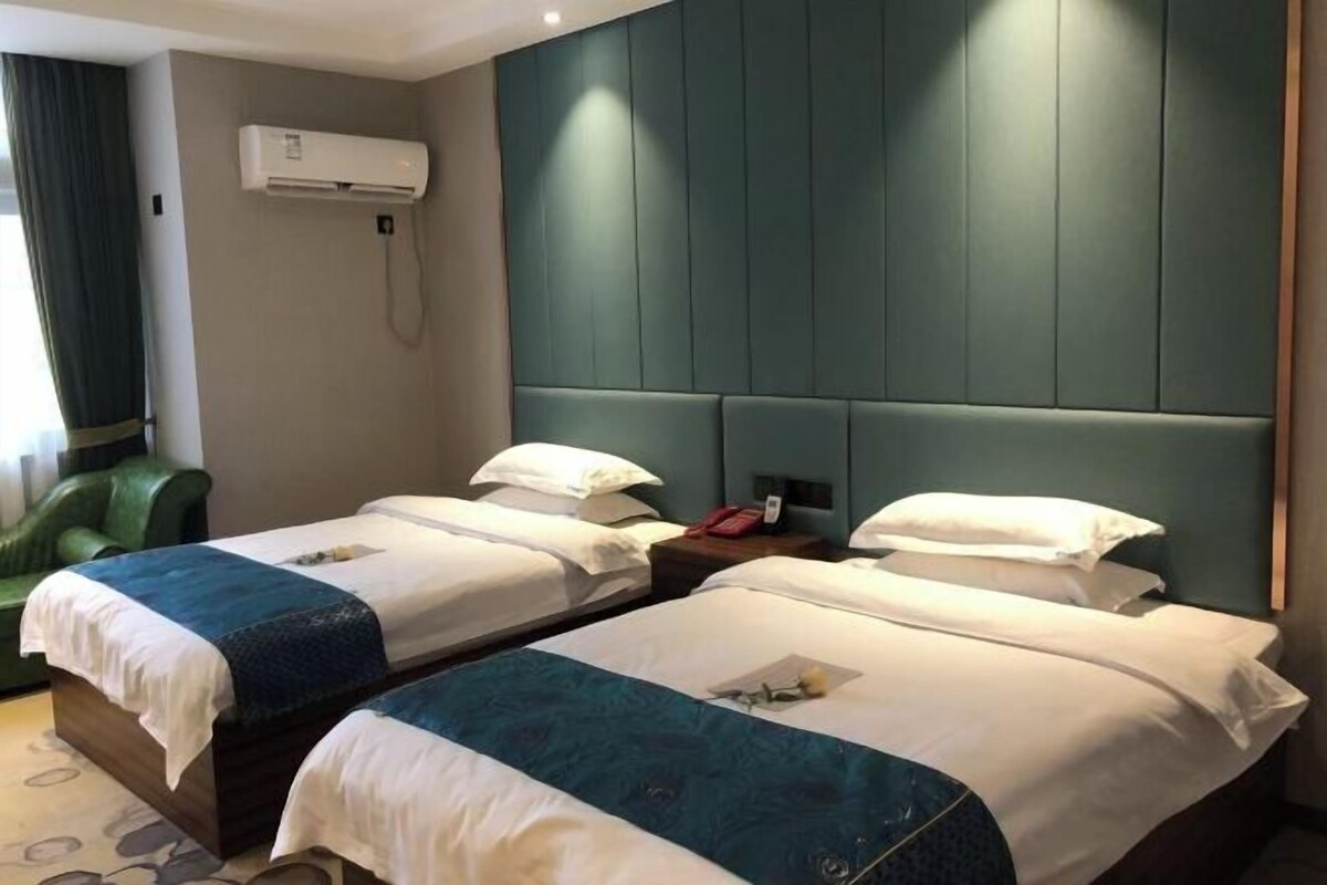 A hotel room with two beds, a green leather chair, an air conditioning unit, and a headboard with vertical panels.