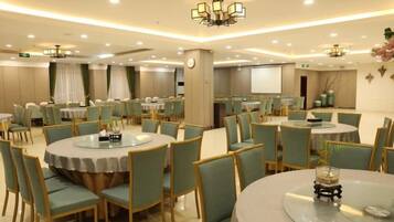 A conference room with multiple tables and chairs, a projector screen, and a clock on the wall.
