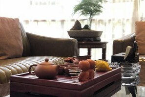A cozy living room with a leather sofa, a wooden tray with tea set, and a bonsai tree. - Yoron Hotel (Nanchang County)