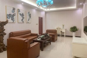 A modern living room with a brown leather sofa, a wooden coffee table, and a white cabinet. There are abstract paintings on the wall and a chandelier.