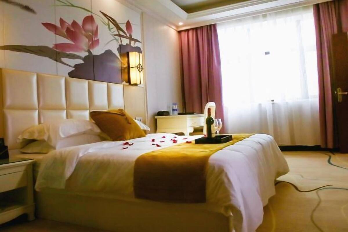 Een hotelkamer met een bed, een nachtkastje, een lamp, een raam met gordijnen en een muur met een bloemschilderij.