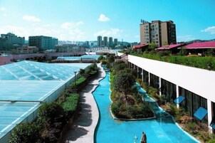 Un área de piscina en la azotea con un invernadero de vidrio, un elemento acuático y una hilera de edificios al fondo.