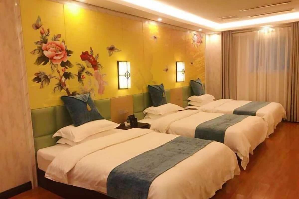 Een hotelkamer met drie bedden, een gele wand met bloemistructuur en twee wandlampen.