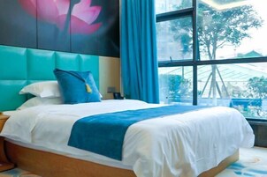 Habitación de hotel con una cama grande, cabecera con diseño floral y ventana con vistas a árboles y un edificio.