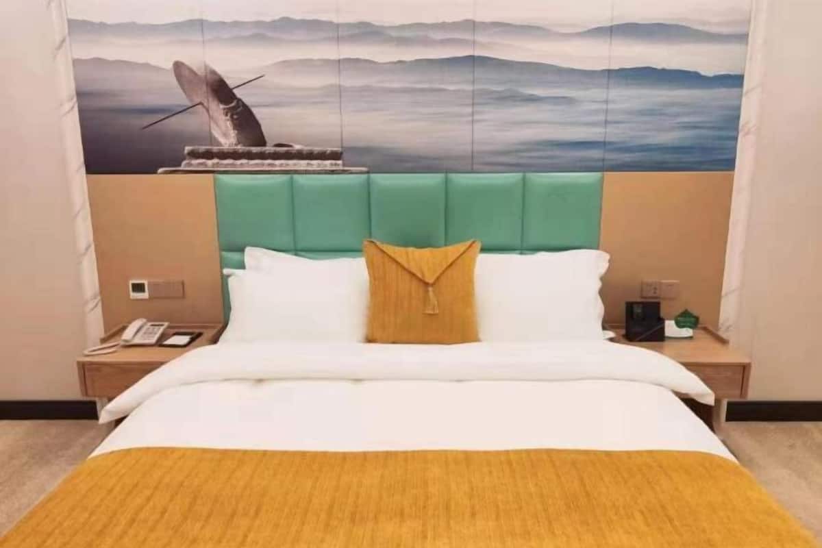 Een hotelkamer met een bed, een nachtkastje, een telefoon en een muur met een berglandschap schilderij.