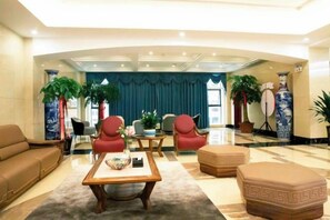 A hotel lobby with a sofa, armchairs, a coffee table, and decorative plants. - Yibo Garden Hotel (Zhenxiong)