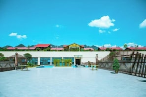 A spacious outdoor area with a pool, surrounded by a fence and buildings with red roofs.