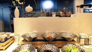 Buffet-alueella on useita erilaisia ruokalajeja tarjoavia kulhoja, viinipullo ja koriste-esineitä.