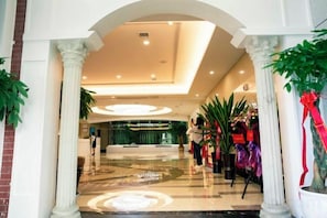 Un vestíbulo de hotel con una recepción, piso de mármol y columnas.