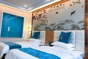A hotel room with two beds, a large window with blue blinds, and a decorative wall with floral and bird paintings.