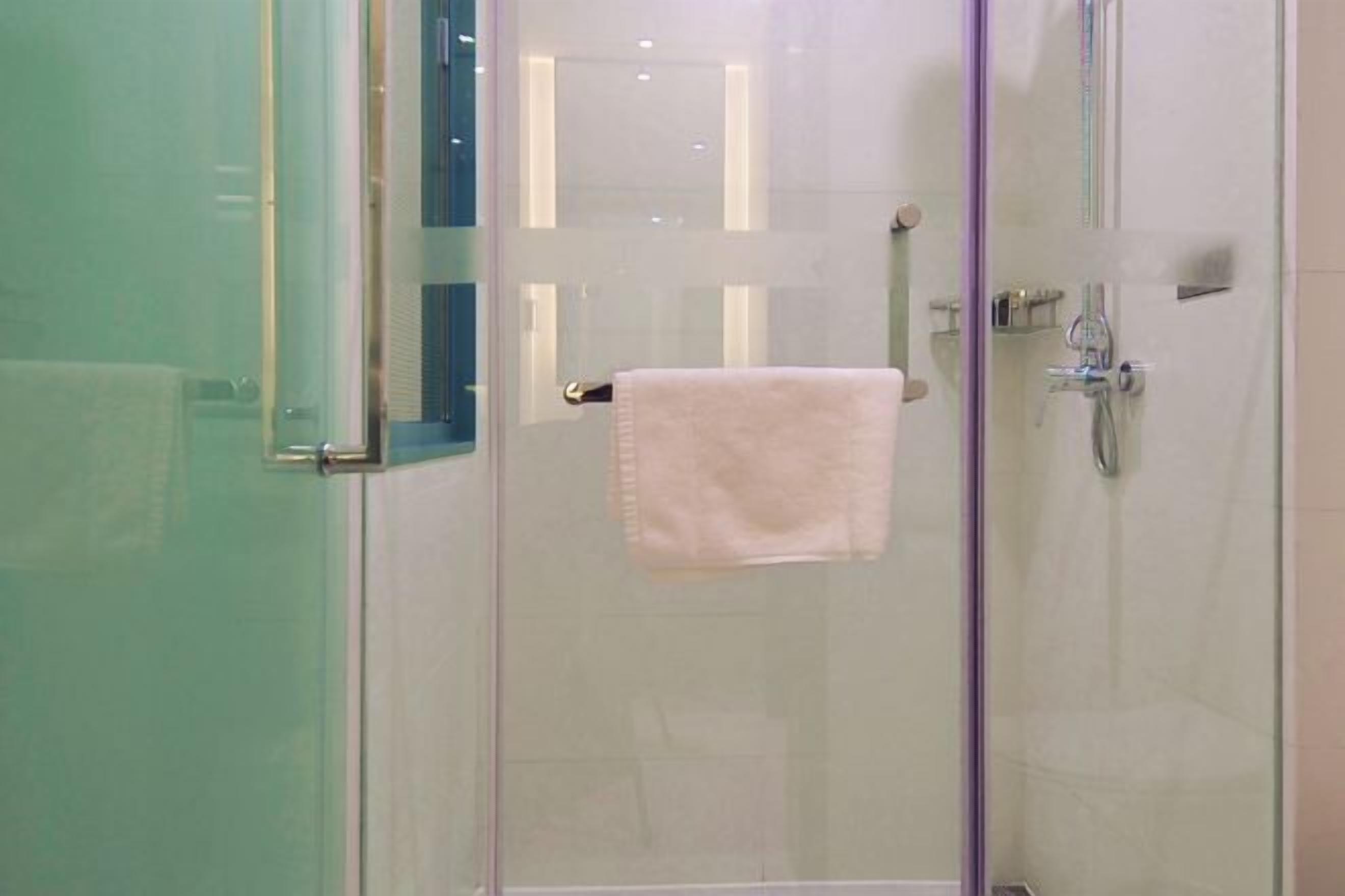 Un espace douche fermé par des parois de verre, avec une serviette visible accrochée à la poignée de la porte.
