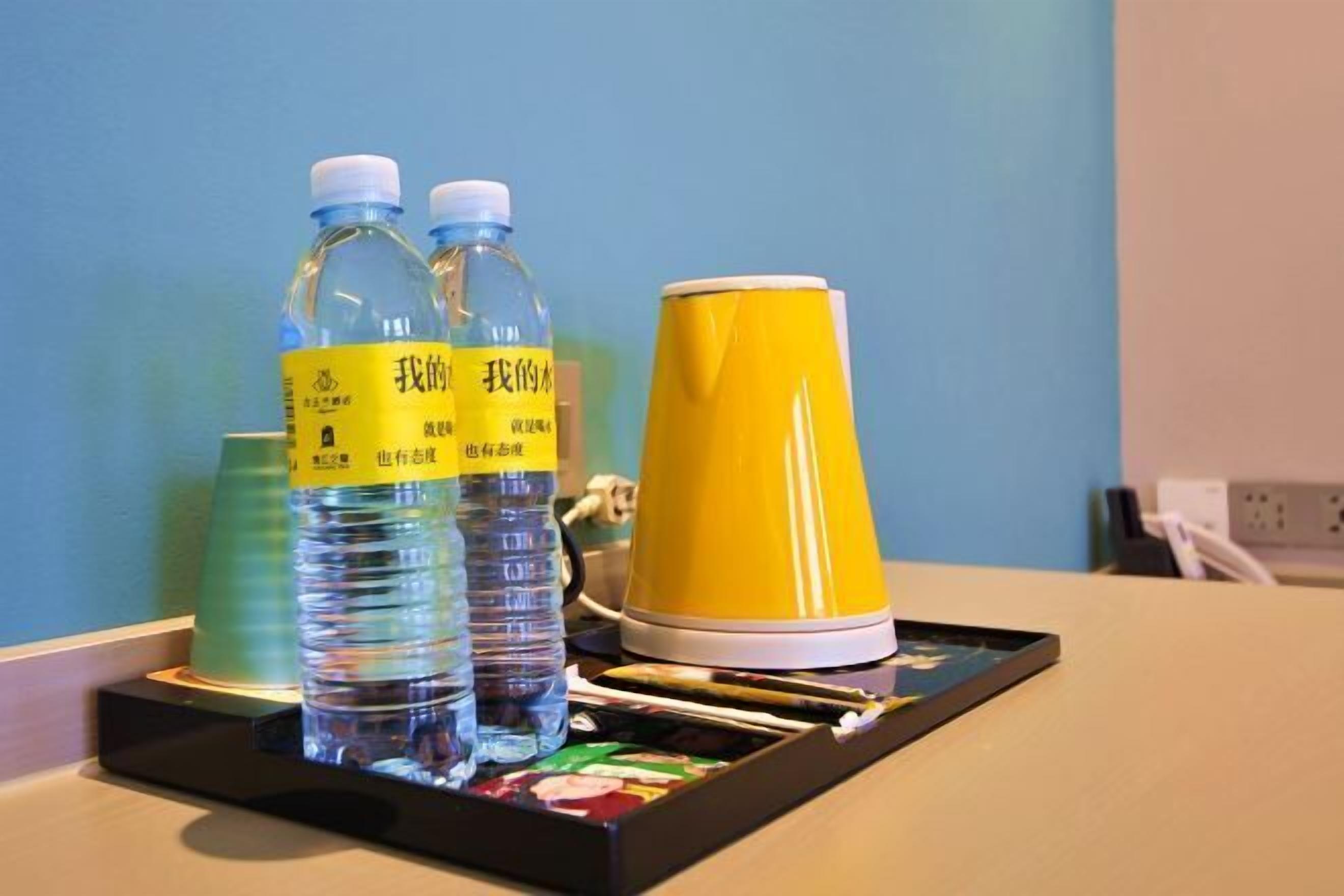 Un plateau avec deux bouteilles d’eau, une tasse jaune et un gobelet vert, posé sur une table.