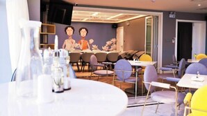 Un comedor moderno con mesas y sillas redondas, un mural en la pared e iluminación empotrada en el techo.
