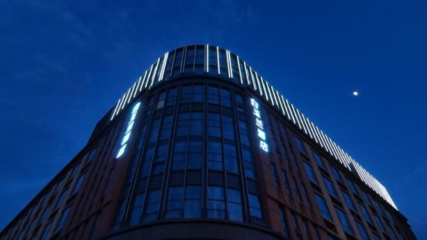 Un edificio moderno con fachada curva y ventanas iluminadas contra un cielo nocturno.