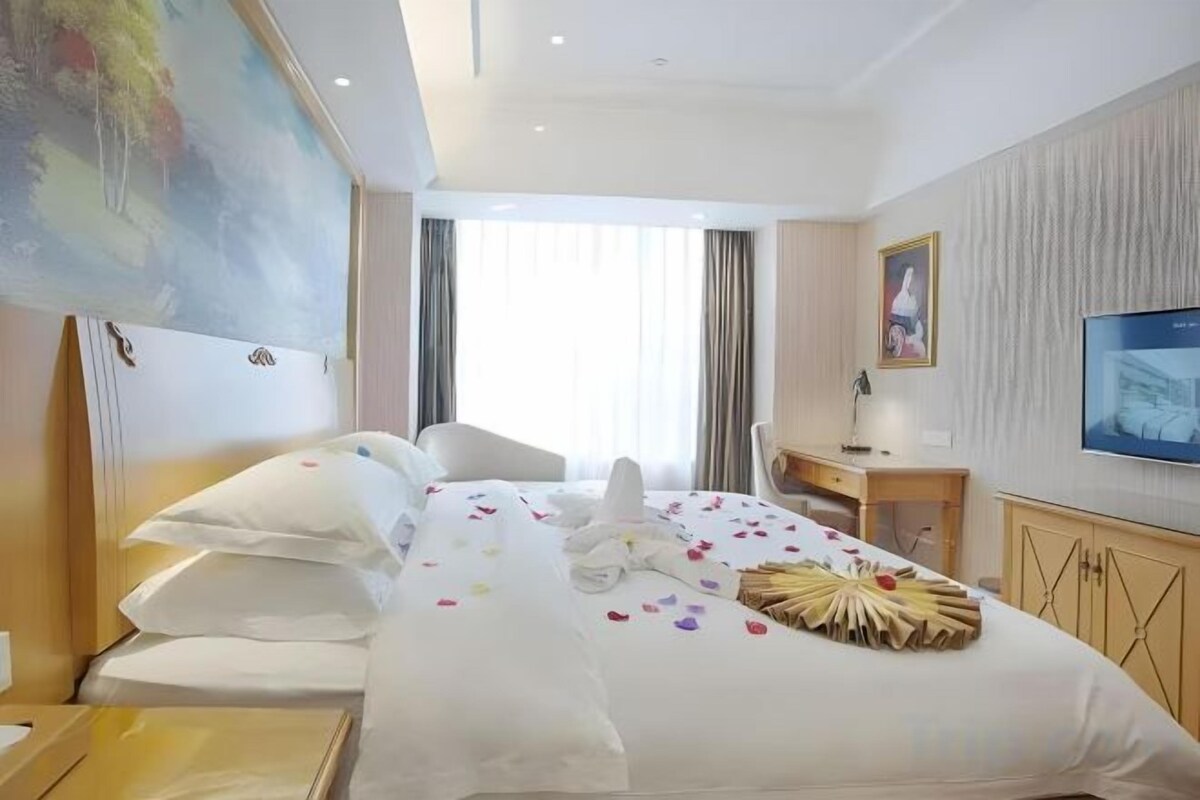 A hotel room with a bed, a desk, a chair, a television, and a painting on the wall.