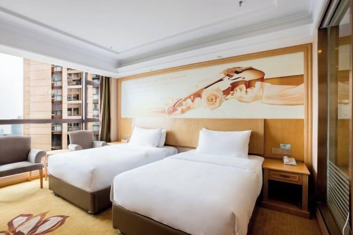 A hotel room with two beds, a sofa, a nightstand, and a large window.