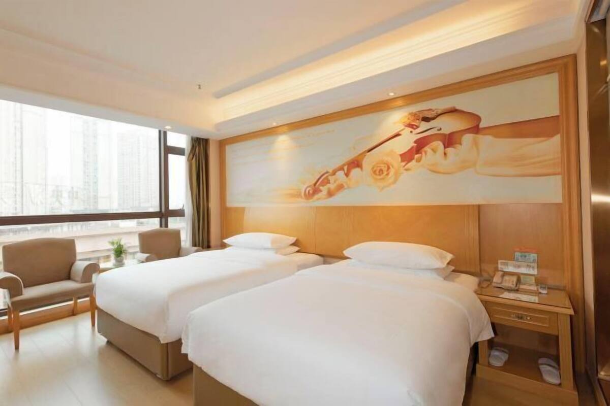 A hotel room with two beds, a sofa, a nightstand, and a large window.