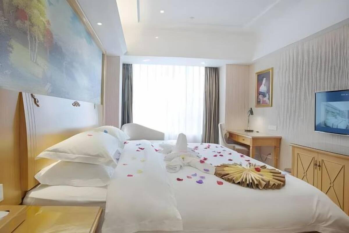 A hotel room with a bed, a desk, a chair, a television, and a painting on the wall.