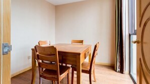 Una habitación con una mesa de madera y cuatro sillas, una puerta con pomo y una ventana con cortinas.