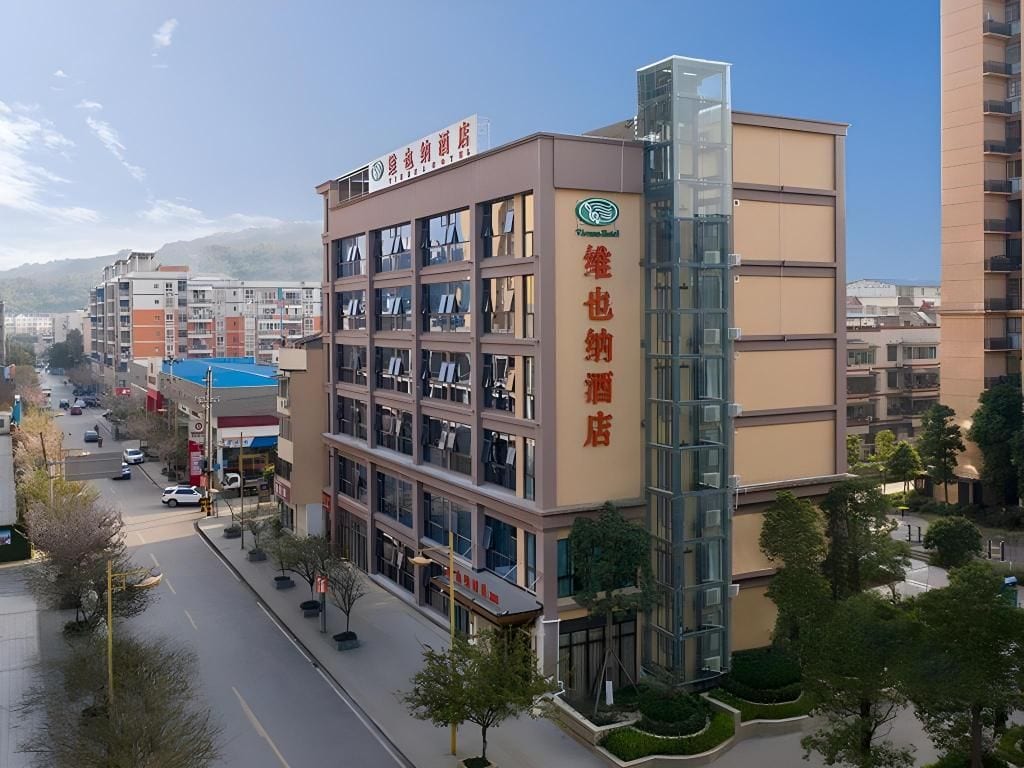A multi-story hotel with a prominent glass elevator shaft, a visible sign indicating a hotel and restaurant, and a clear view of the surrounding urban area.