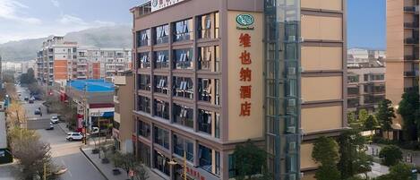 A multi-story hotel with a prominent glass elevator shaft, a visible sign indicating a hotel and restaurant, and a clear view of the surrounding urban area.