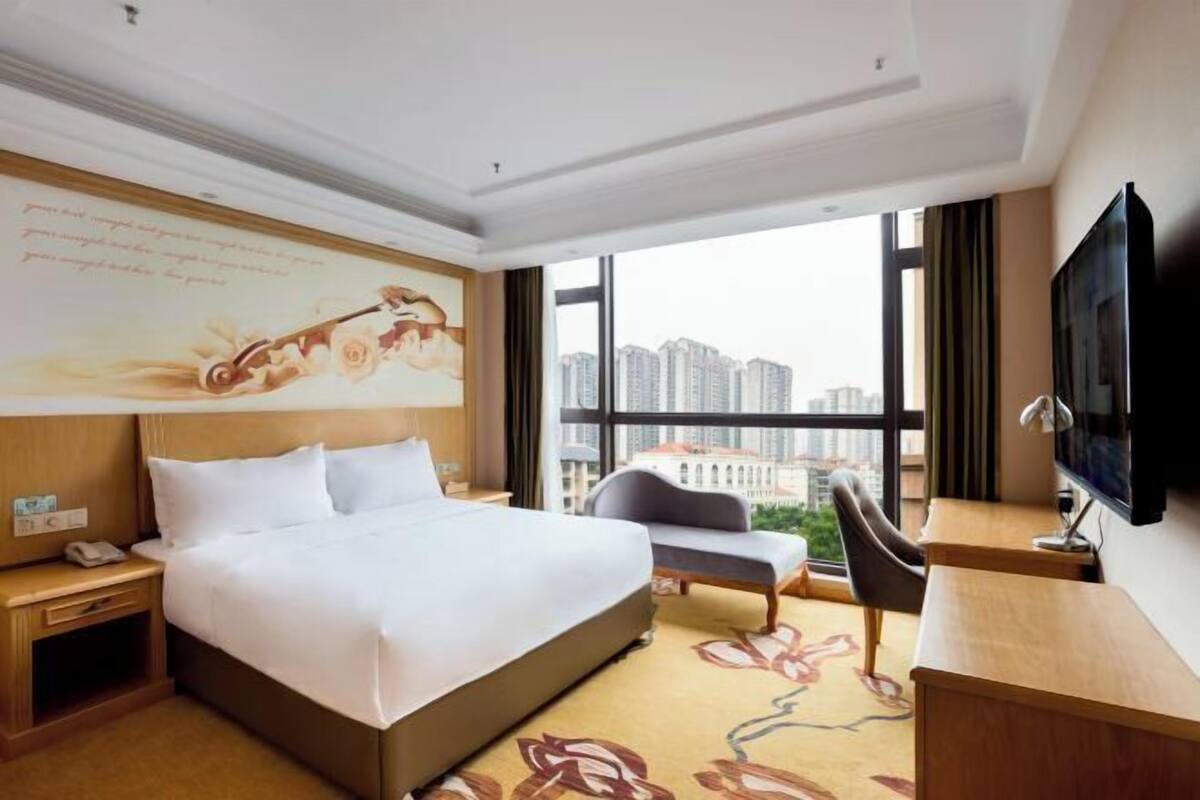 A hotel room with a large bed, a desk, a chair, and a TV.
