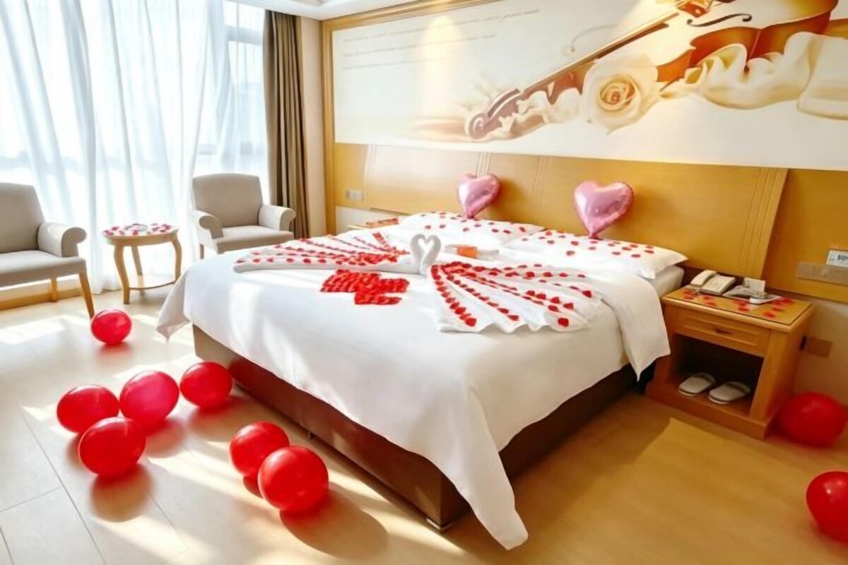 A hotel room with a bed, bedside tables, a nightstand, and a large window.