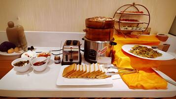 A breakfast buffet with various food items, a coffee maker, and a hot pot on a table.