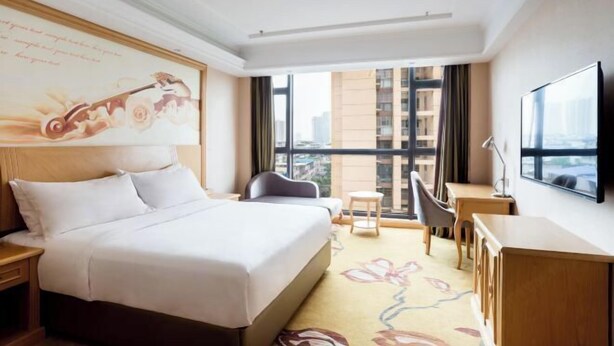 Habitación de hotel con una cama grande, un escritorio, una silla, un televisor y una ventana con vista a la ciudad.
