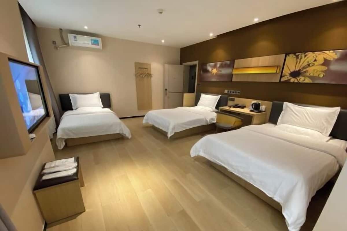 Une chambre d’hôtel avec trois lits, un téléviseur à écran plat, une machine à café et une œuvre d’art accrochée au mur.