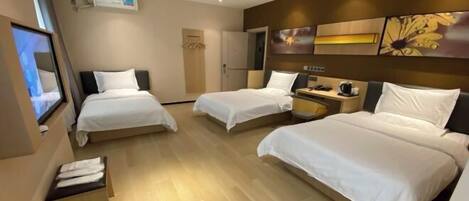 A hotel room with three beds, a flat-screen TV, a coffee machine, and a wall-mounted artwork.