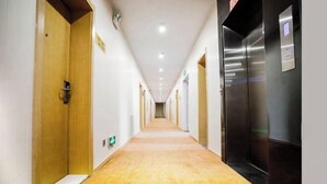 A hotel hallway with wooden doors, a carpeted floor, and a modern elevator. - Jucheng Youpin Hotel (Ju County)
