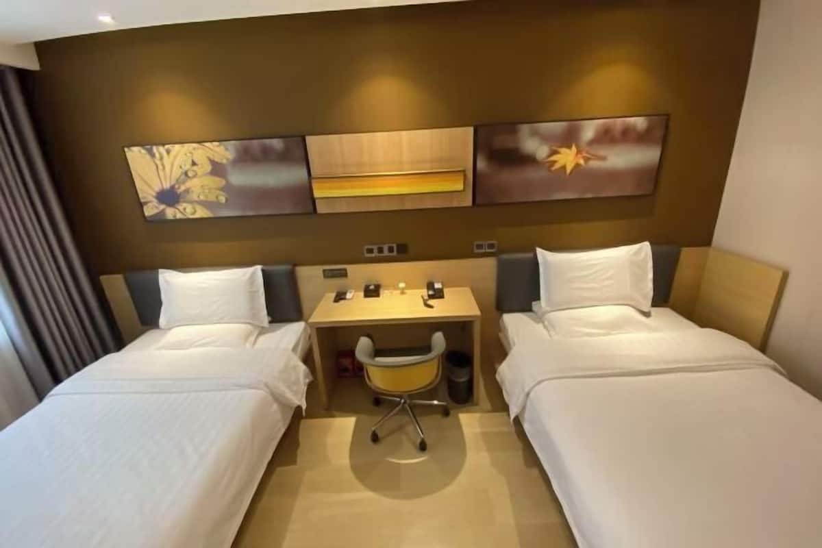 Une chambre d’hôtel avec deux lits, un bureau et une chaise. Trois œuvres d’art sont accrochées au mur, au-dessus du bureau.