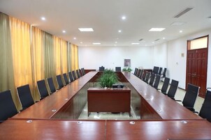Un salón de conferencias con una larga mesa, sillas y una planta.