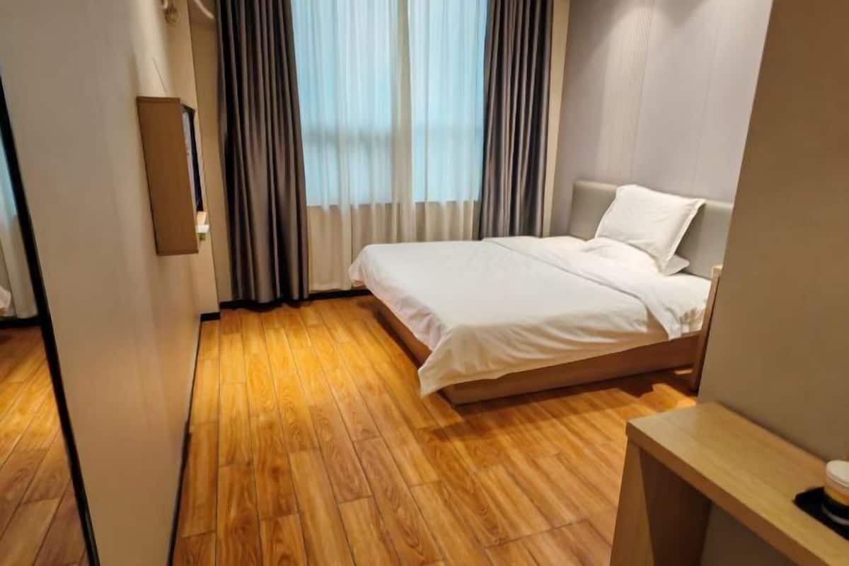 Une chambre d’hôtel avec un plancher en bois, un lit avec une literie blanche, une table de chevet et une fenêtre avec des rideaux.