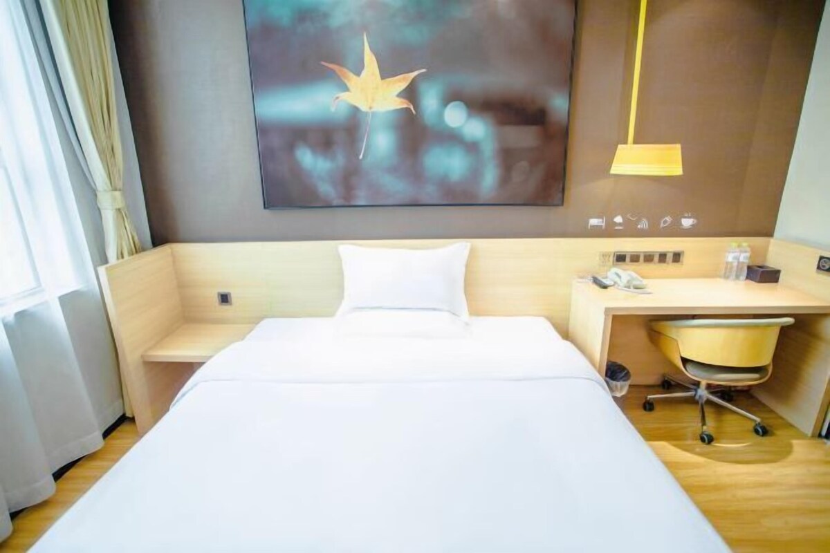 A hotel room with a bed, a desk, a chair, a lamp, and a wall-mounted phone.