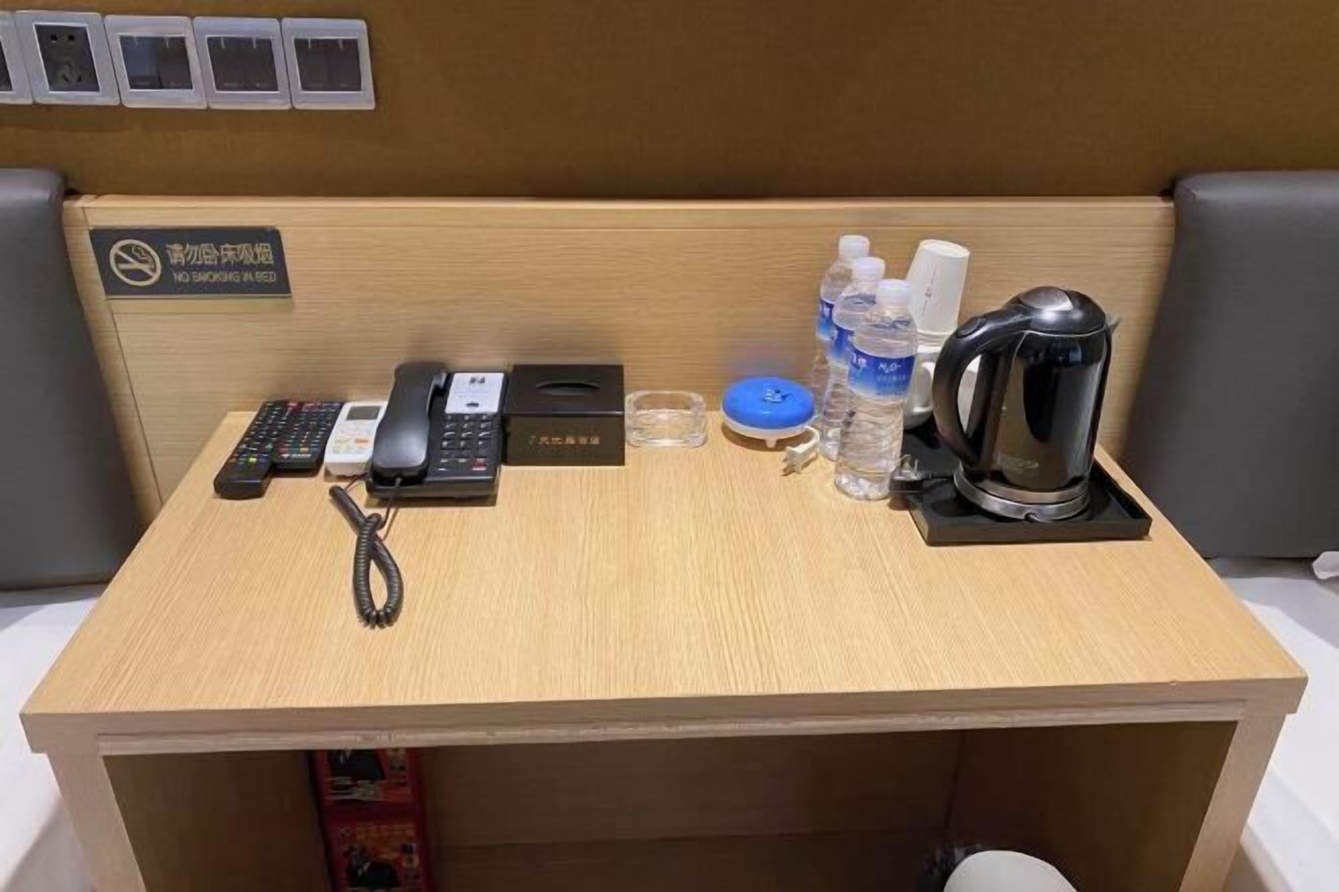 A hotel workspace with a desk, telephone, coffee maker, water bottles, and a sign indicating no smoking.