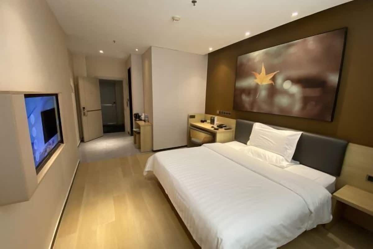 Une chambre d’hôtel moderne dotée d’un grand lit, d’un téléviseur à écran plat, d’un bureau et d’un grand tableau abstrait accroché au mur.