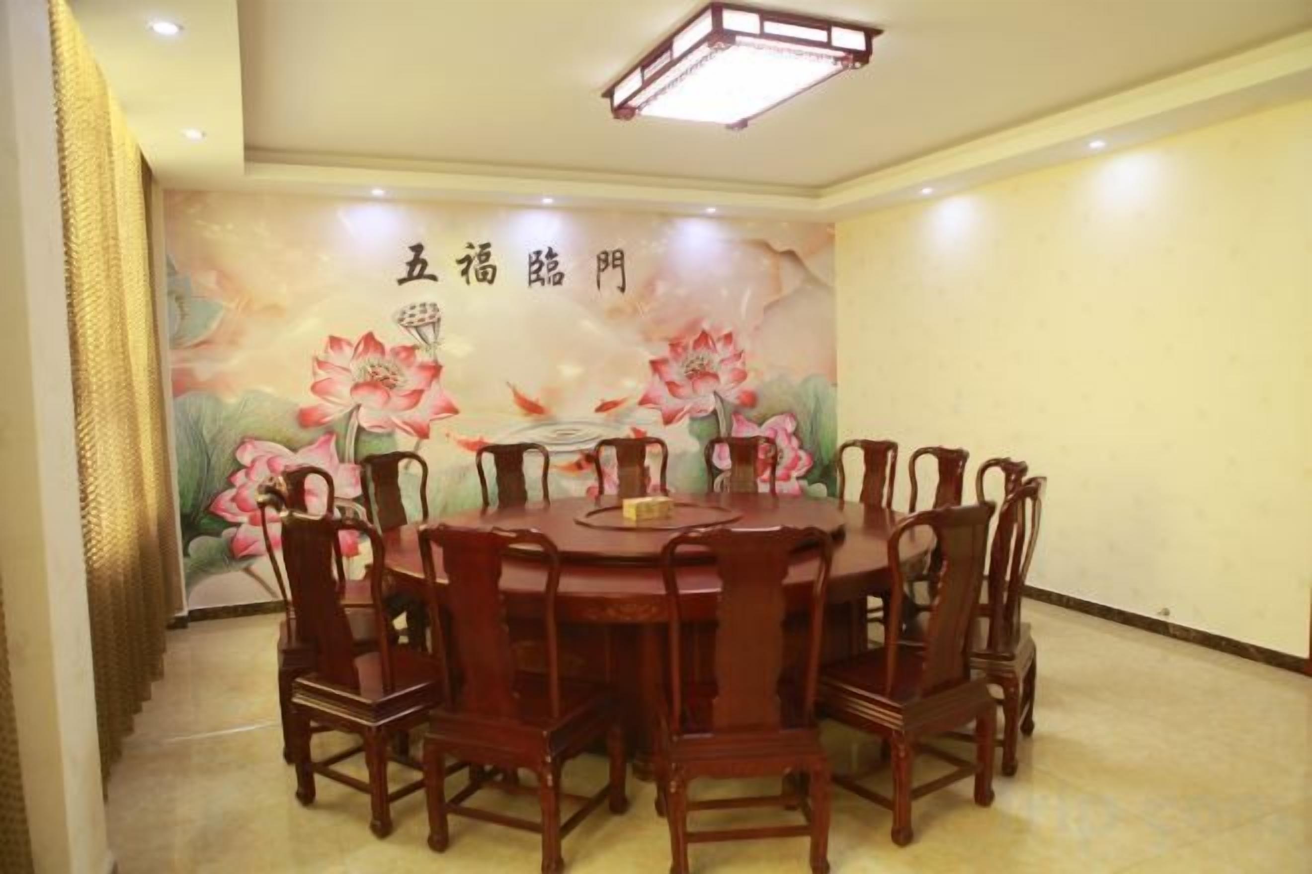 Un salón de conferencias con una mesa redonda y sillas, un mural en la pared con motivos florales y una lámpara en el techo.