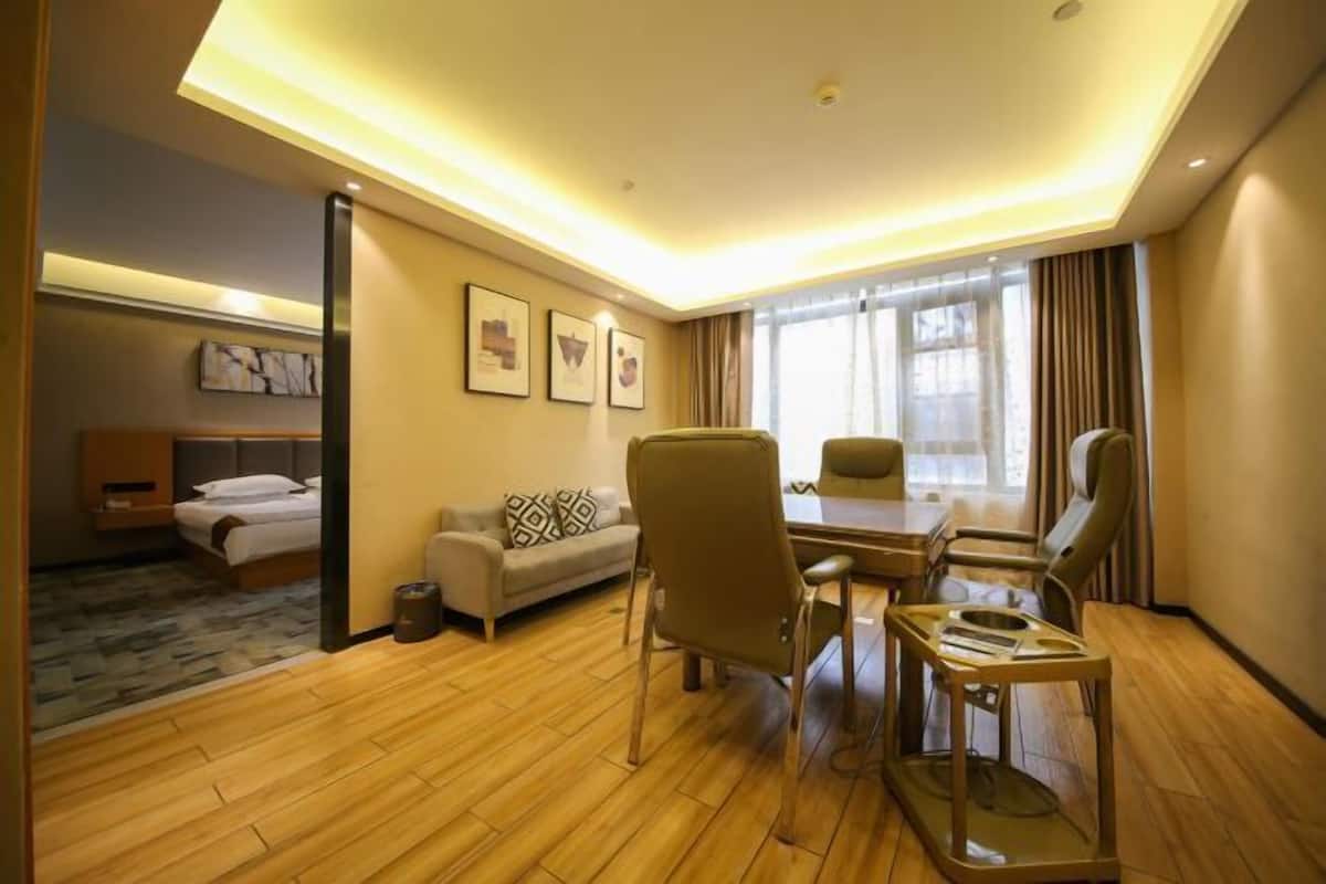 Una habitación de hotel con una cama, un sofá, una mesa de comedor con sillas, una mesita con tapa de vidrio y una ventana con cortinas.