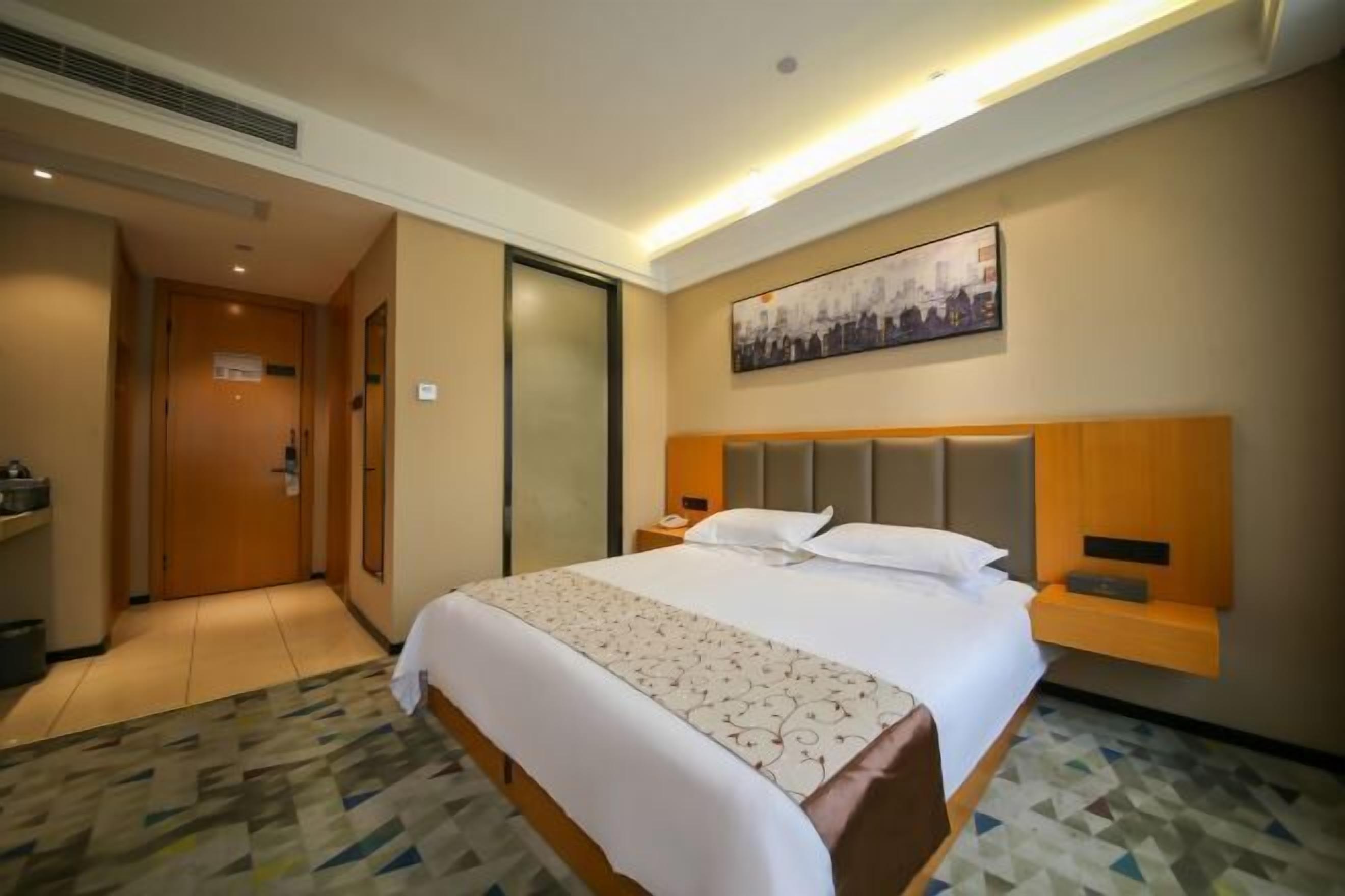A hotel room with a large bed, a headboard, bedside tables, a nightstand, a wall-mounted artwork, and a patterned carpet.