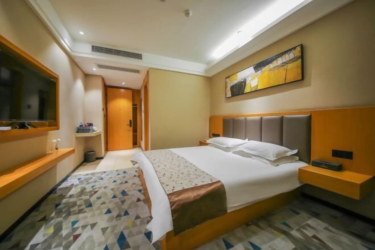 A hotel room with a large bed, a television, a painting on the wall, and a patterned rug.