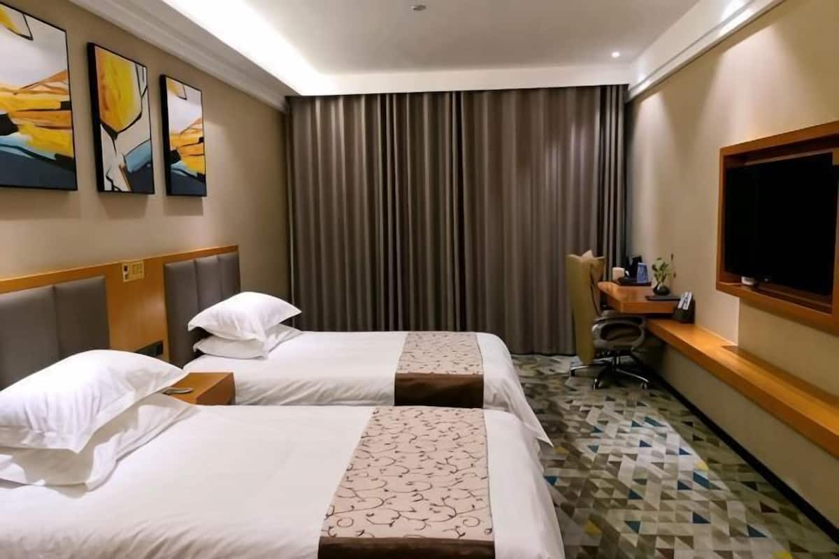 Habitación de hotel con dos camas, un escritorio, un televisor y un ventanal grande con cortinas.