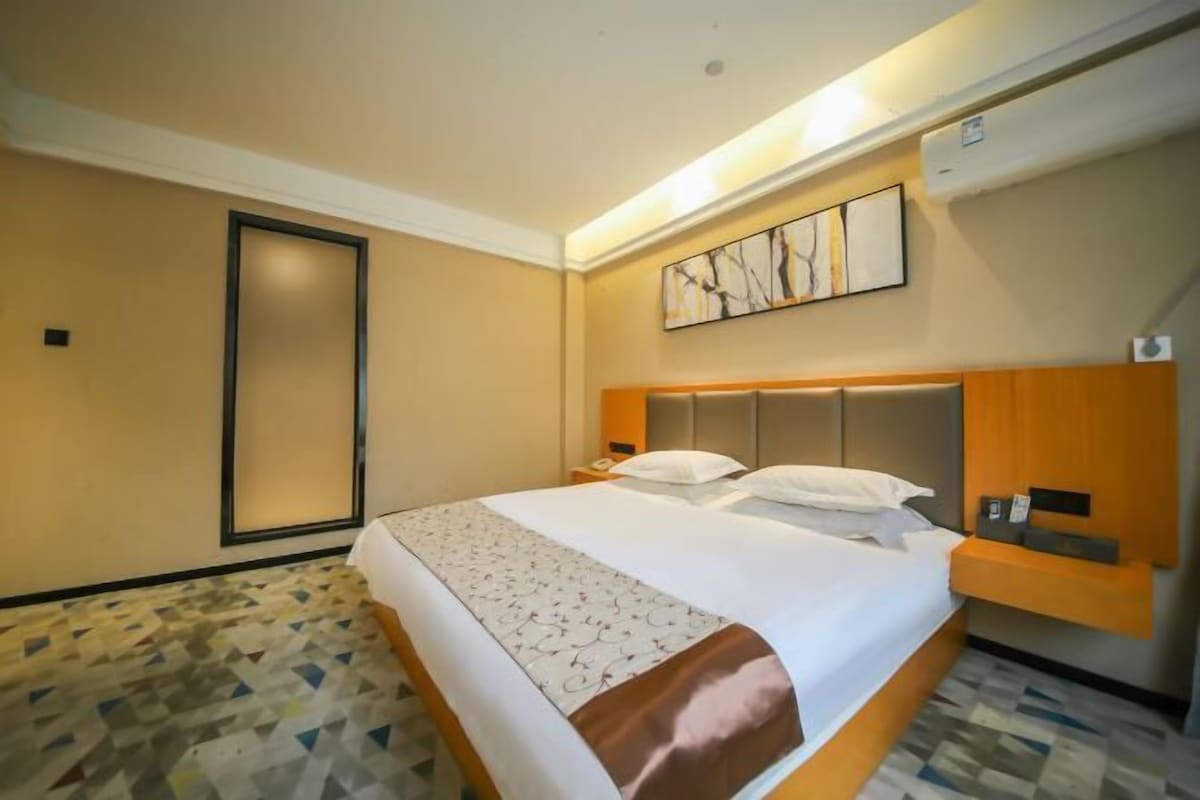 A hotel room with a large bed, a headboard, a bedside table, and a wall-mounted artwork.