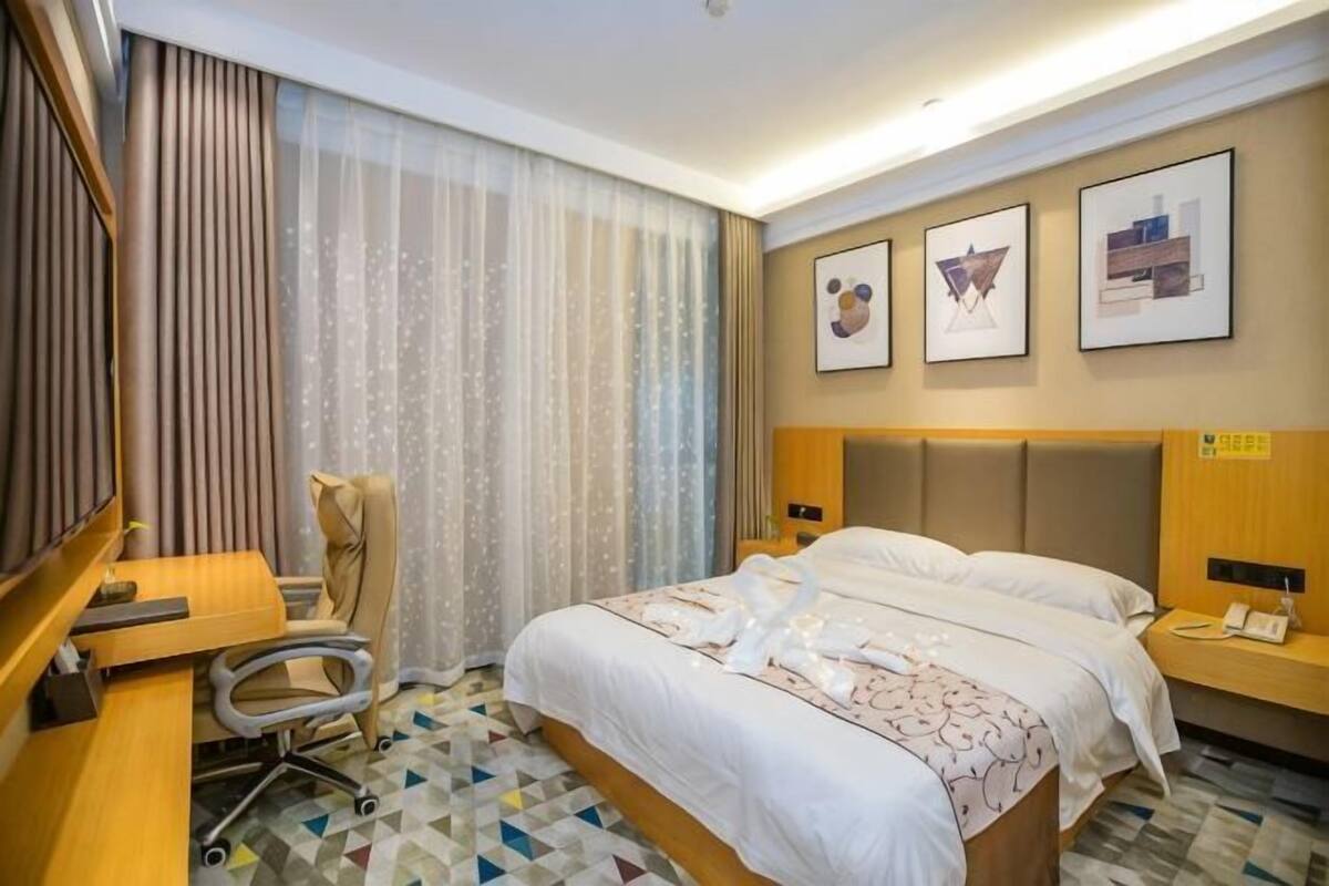 Habitación de hotel con cama, escritorio, silla y cortinas.