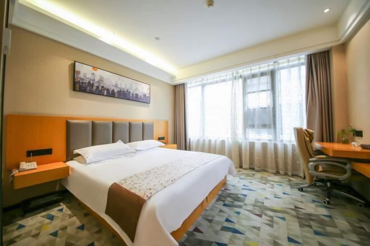 Habitación de hotel con una cama grande, un escritorio y una silla. Hay un cuadro en la pared y una ventana con cortinas.