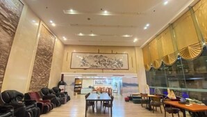 Un amplio vestíbulo de hotel con una larga mesa de comedor, varias sillas y una fila de sofás de cuero negro.